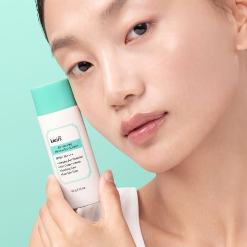 KLAIRS  All Day Airy Invisible Tone-Up Sunscreen 60g (SPF50+ PA++++), tube tenu près du visage sur fond bleu.