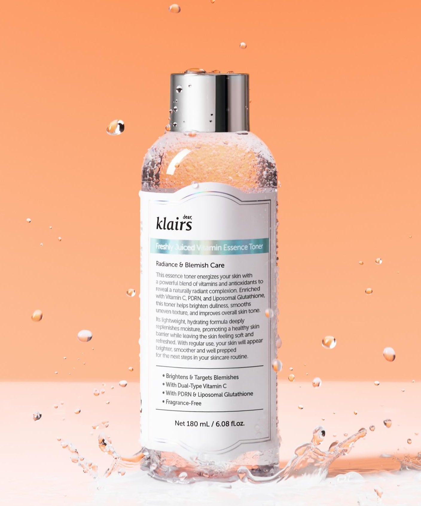 KLAIRS Freshly Juiced Vitamin Blemish Toner 180ml, flacon présenté sur fond orange avec éclaboussures d'eau