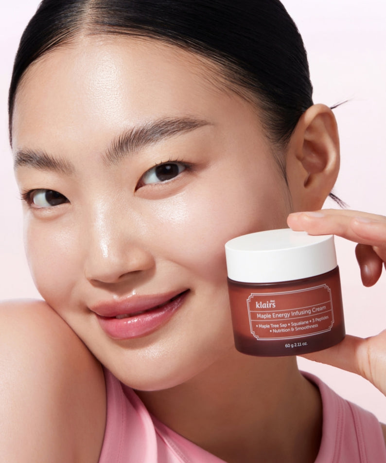 Femme souriante tenant un pot de KLAIRS Maple Energy Infusing Cream 60g devant un fond rose.