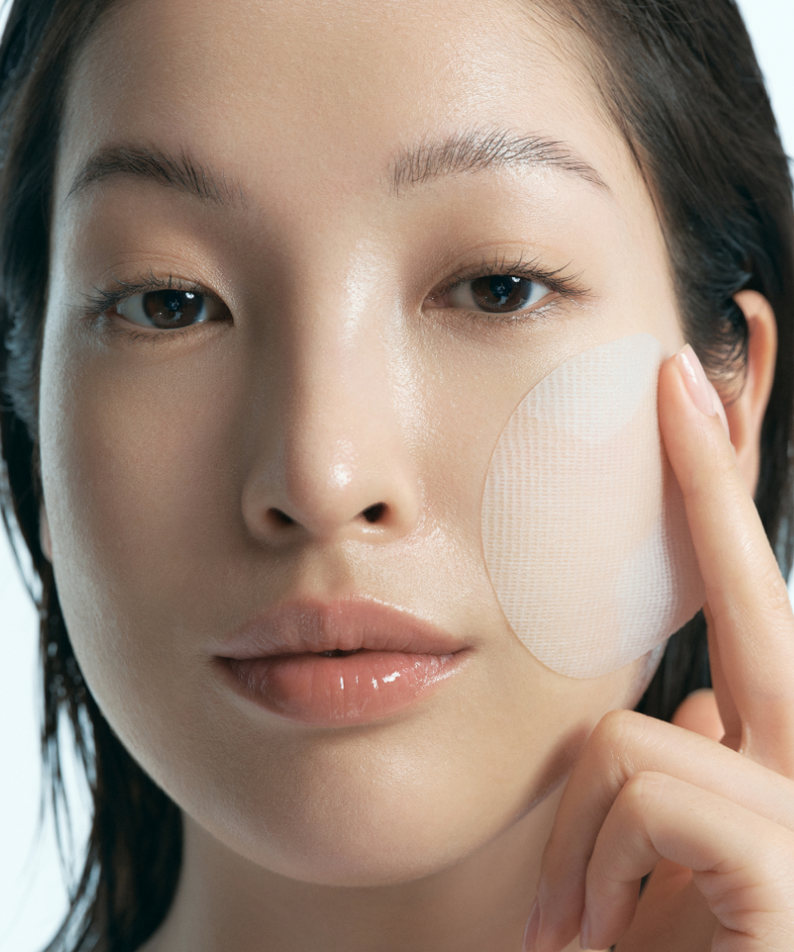 Femme appliquant KLAIRS EGF Blue Calming Toner Pads 60 Pads sur la joue, soin apaisant pour la peau.