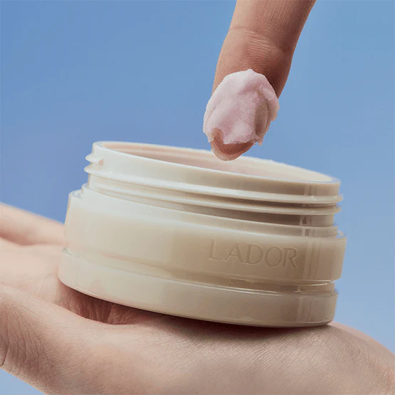 Main tenant LADOR Body Multi Balm 30g de LADOR, pot crème corporel sur fond bleu, texture appliquée