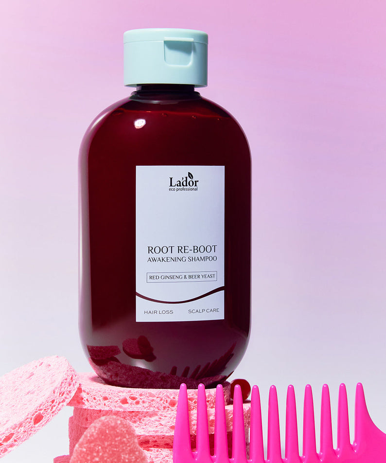Décris l'image en français : LADOR Root Reboot Custom Hair Loss Shampoo 4 Types, flacon Lador violet sur fond rose, brosses.