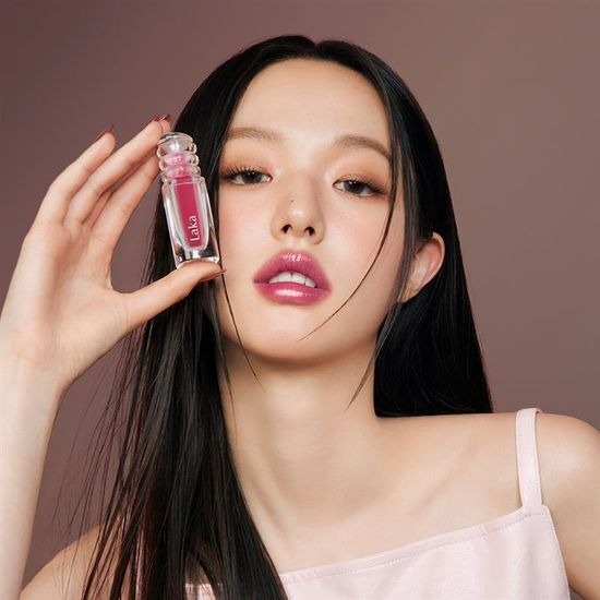 LAKA Maxi Glare Tint, produit LAKA, femme en gros plan tenant le flacon sur fond rose, maquillage lumineux