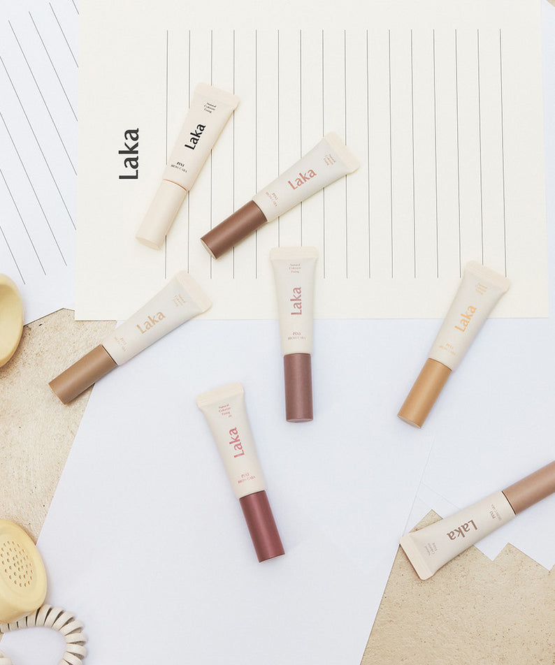 LAKA Pixi Brow Cara 8g, tubes de maquillage LAKA sur fond clair avec textures, accessoires et lumière naturelle.