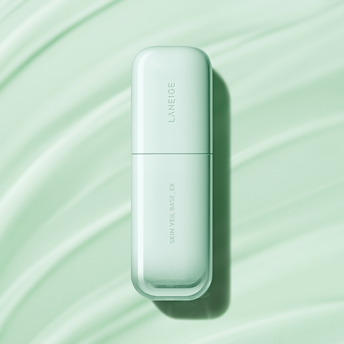 LANEIGE Skin Veil Base SPF28/PA++ 30ml, flacon blanc sur fond vert à rayures, mise en scène maquillage.