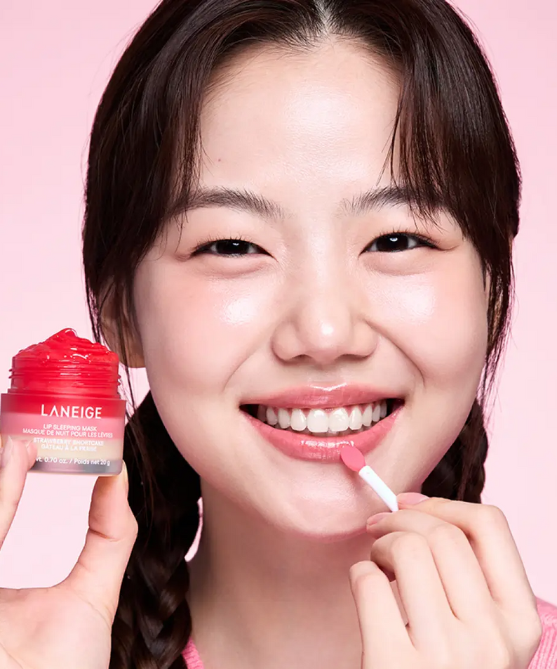 Femme appliquant LANEIGE Lip Sleeping Mask EX Strawberry Shortcake 20g avec sourire éclatant sur fond rose.