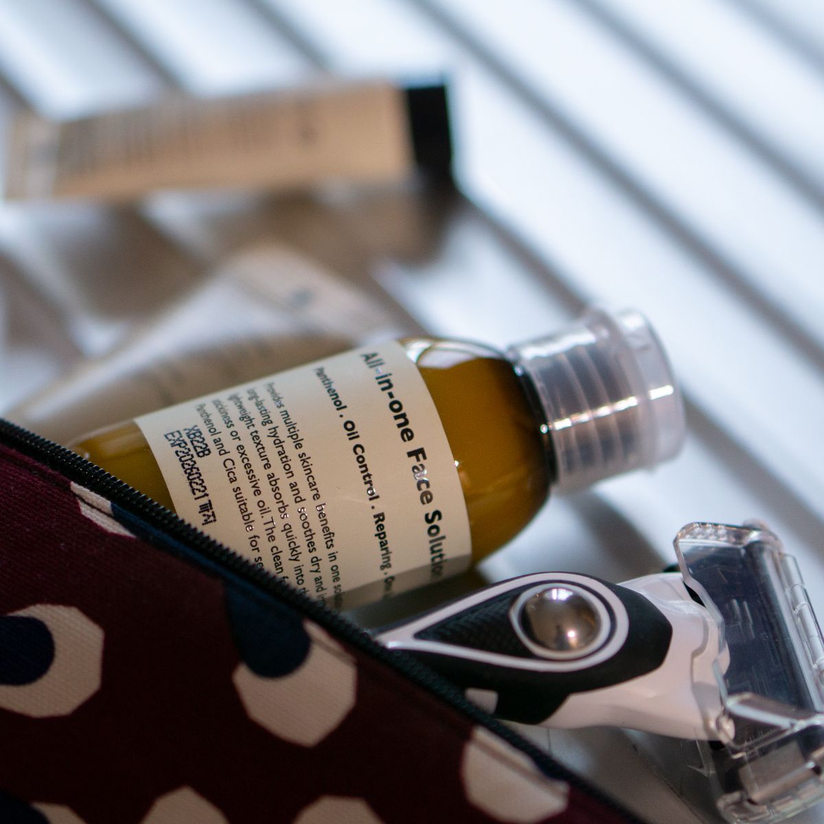 LAZY SOCIETY ALl-in-One Face Solution 50ml de la marque Lazy Society, flacon sur table avec trousse, arrière-plan bleu.