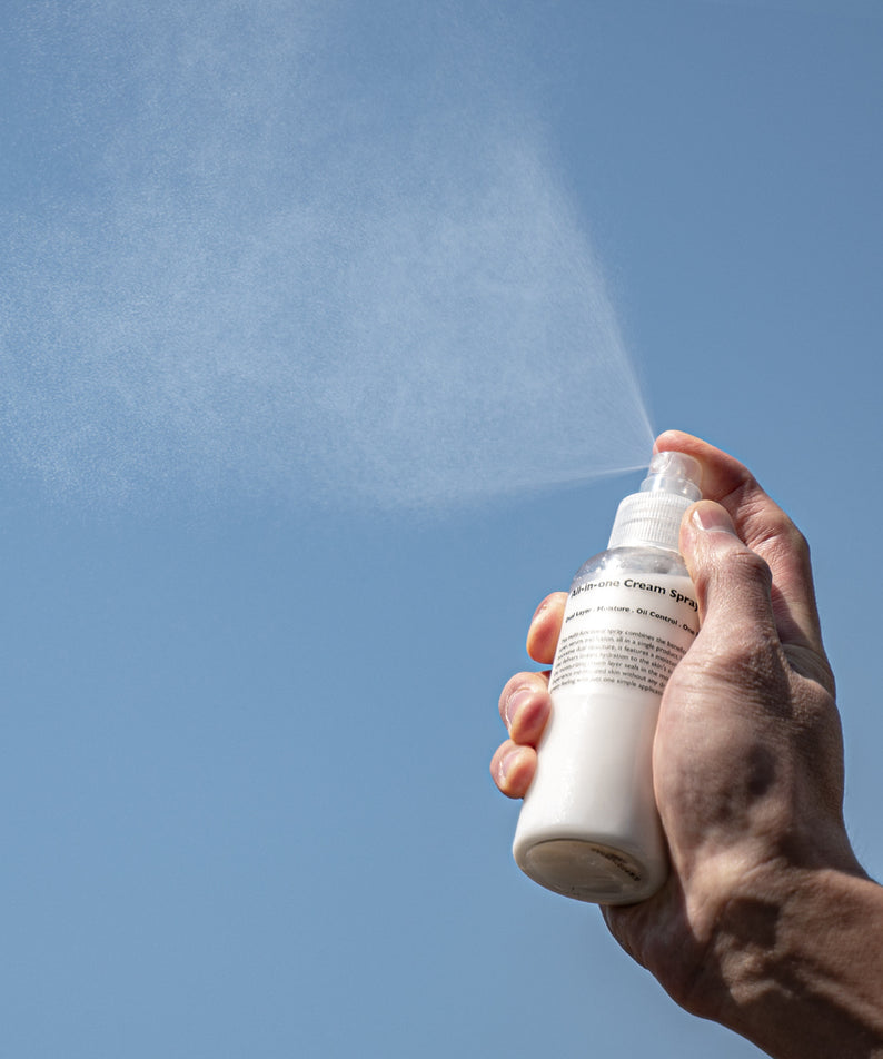LAZY SOCIETY All-in-One Cream Spray 120ml, main tient le spray et projette une brume de crème, fond bleu.