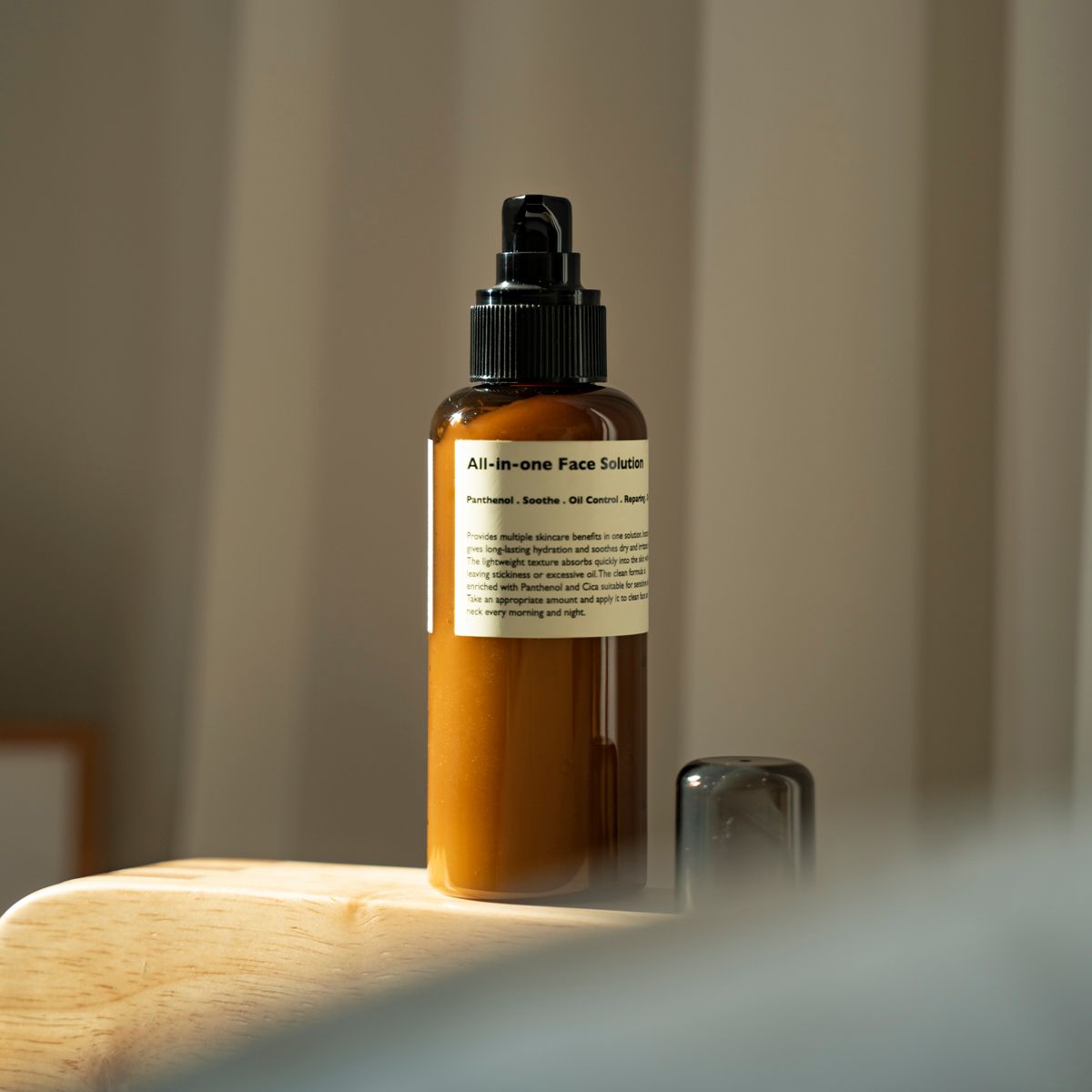 LAZY SOCIETY All-in-One Face Solution 150g, flacon pompe en verre ambré sur table bois, salle de bain, fond flou.