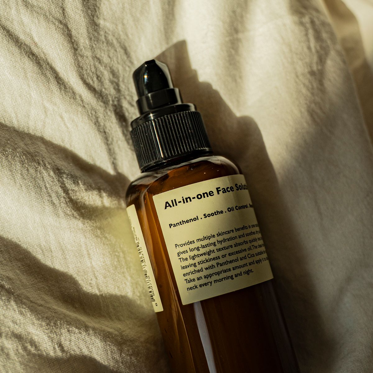 LAZY SOCIETY All-in-One Face Solution 150g, flacon en verre sur linge beige, lumière naturelle, marque au label lisible.