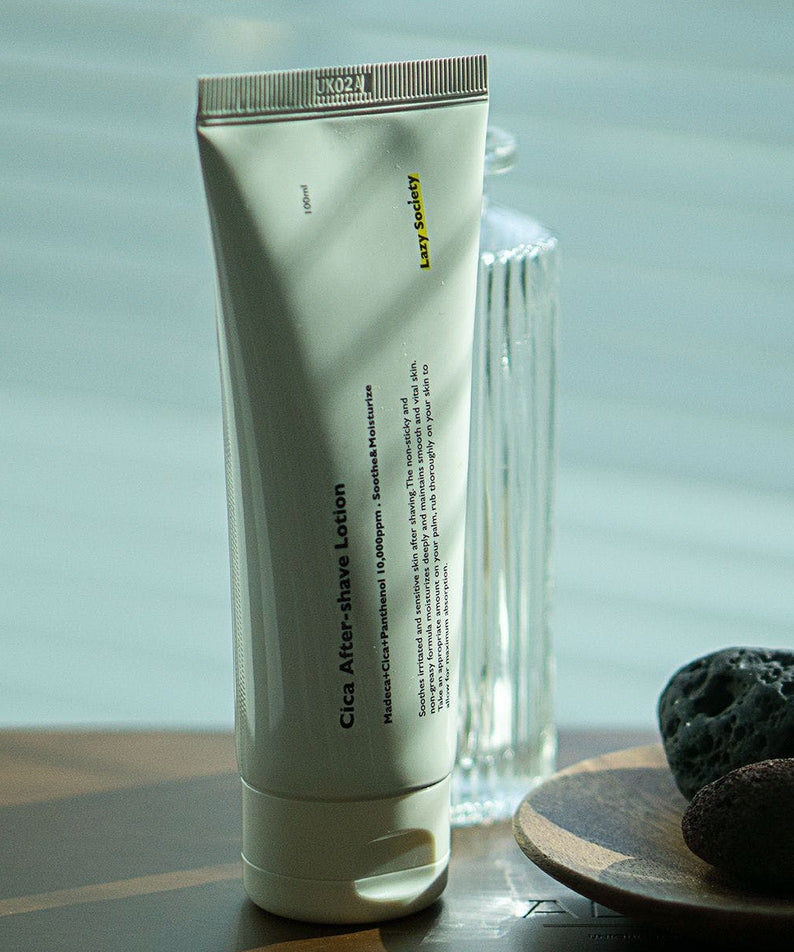 LAZY SOCIETY Cica Aftershave Lotion 100ml en tube vert sur fond spa, pierres et serviette, crème apaisante.