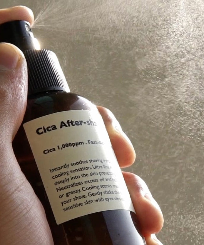 LAZY SOCIETY Cica Aftershave Toner Spray 120ml, main tenant le flacon sur fond texturé, étiquette lisible