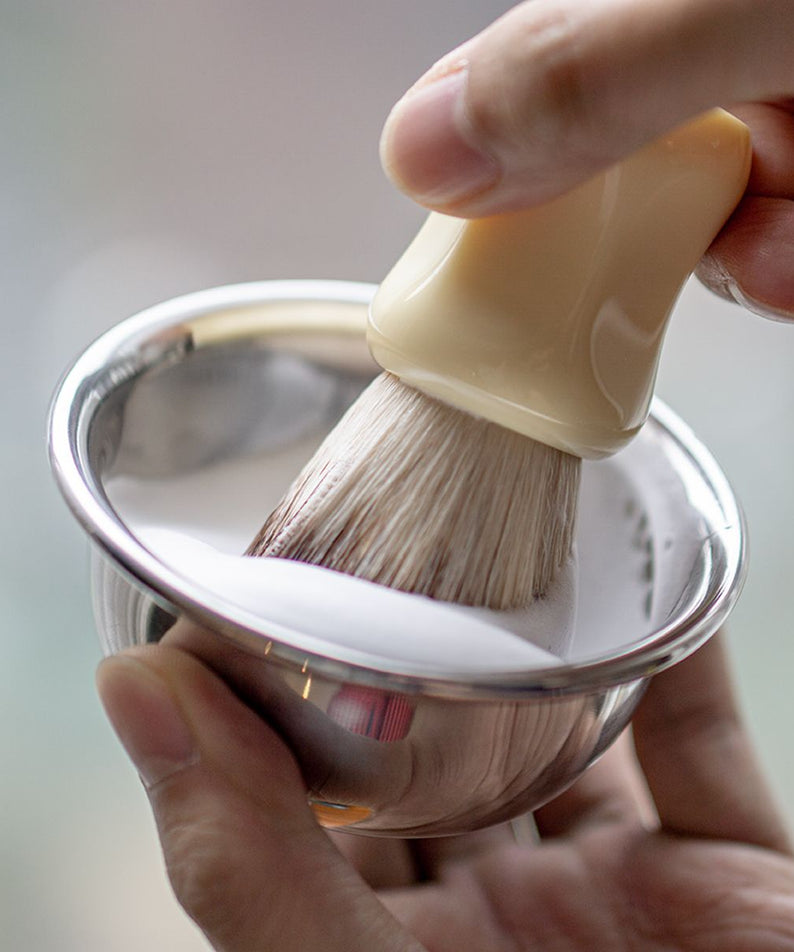 LAZY SOCIETY Classic Shaving Brush, main tenant un blaireau en mousse dans un bol d’atelier, vue rapprochée.