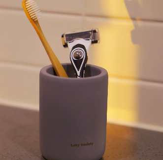 LAZY SOCIETY Diatomaceous Earth Holder 2.0 : porte-ustensiles gris sur plan de salle de bain, brosse à dents, marque visible.