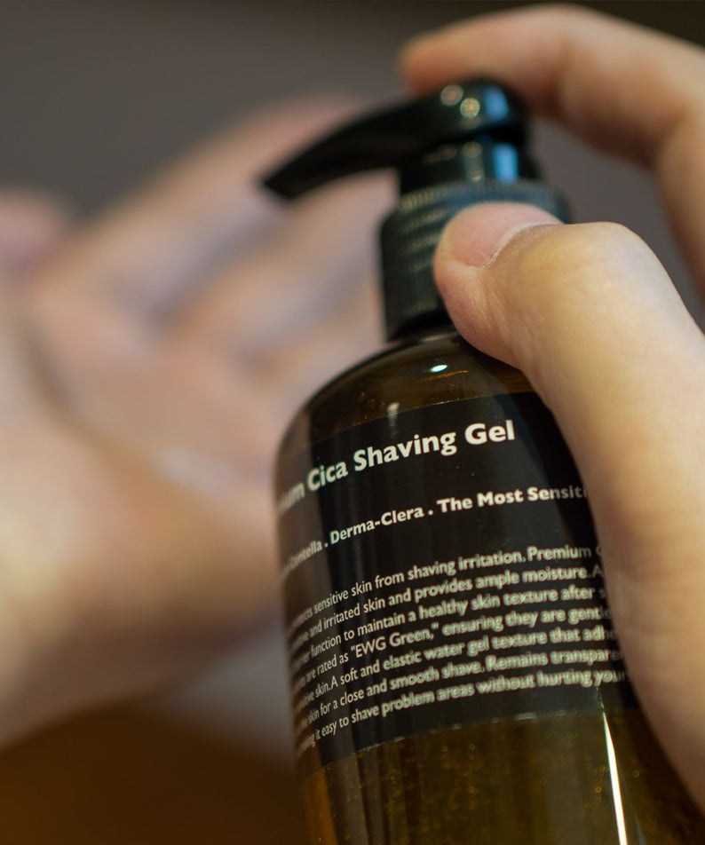 LAZY SOCIETY Premium Cica Shaving Gel 300ml : flacon en main, gel de rasage à la cica, salle de bain floue.