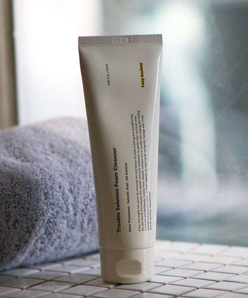 LAZY SOCIETY Trouble Solution Foam Cleanser 120ml, photo du tube sur salle de bain, serviette et décor minimaliste.