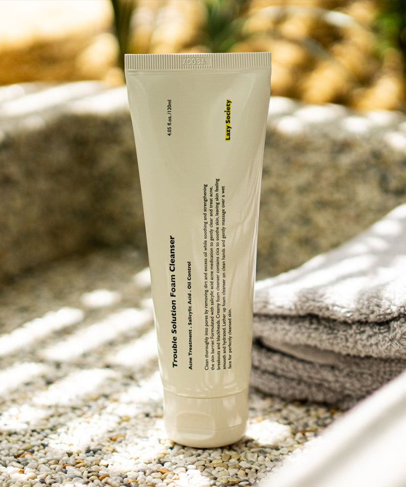 LAZY SOCIETY Trouble Solution Foam Cleanser 120ml, tube de nettoyant visage sur serviette, décor extérieur au coucher du soleil.