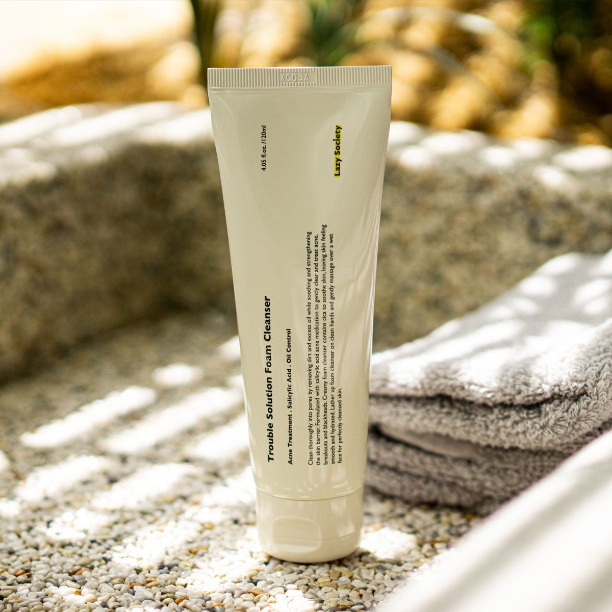 LAZY SOCIETY Trouble Solution Foam Cleanser 120ml, tube de nettoyant visage sur serviette, décor extérieur au coucher du soleil.