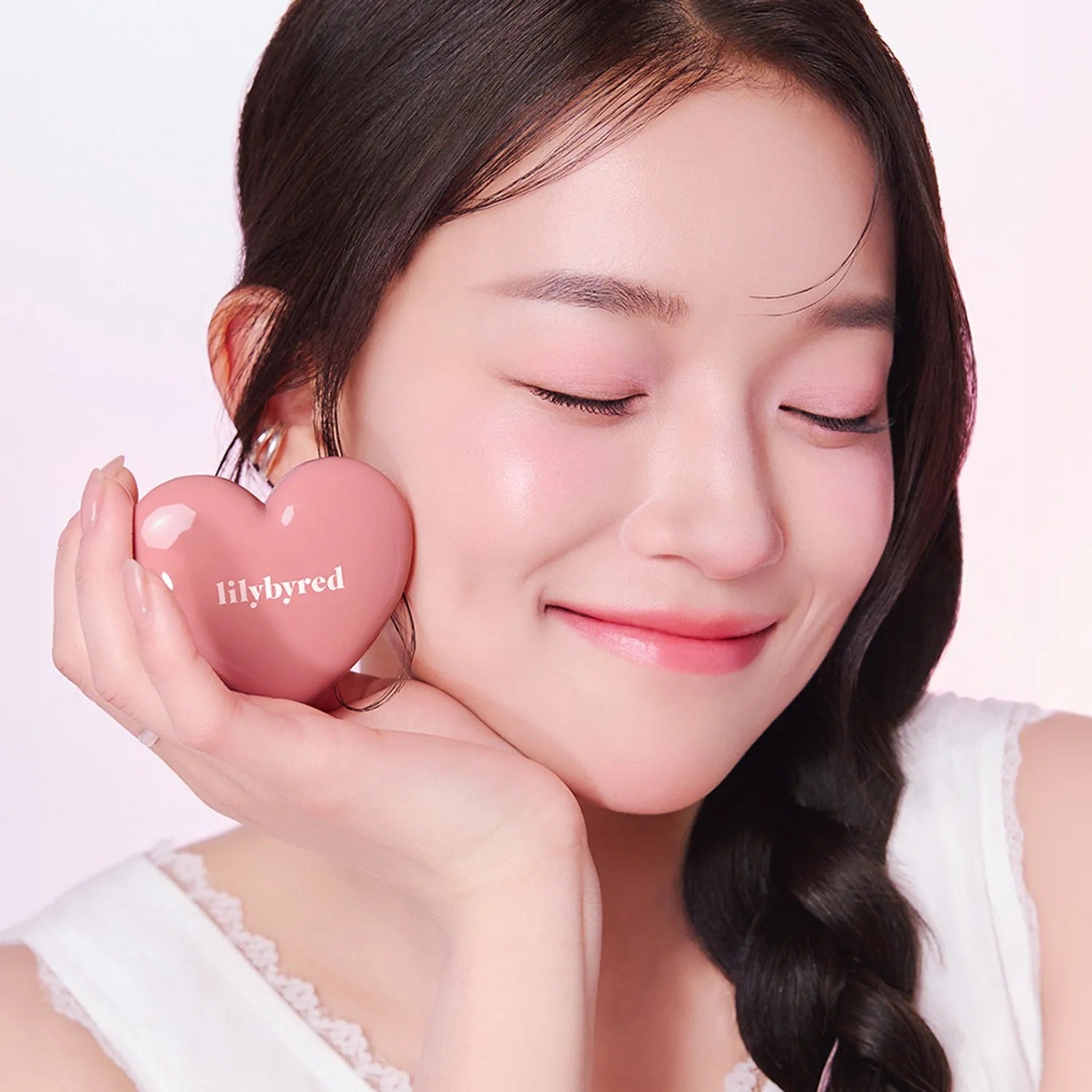 LILYBYRED Love Beam Cheek Balm de la marque LILYBYRED, femme au maquillage appliqué, flacon en forme de cœur rose