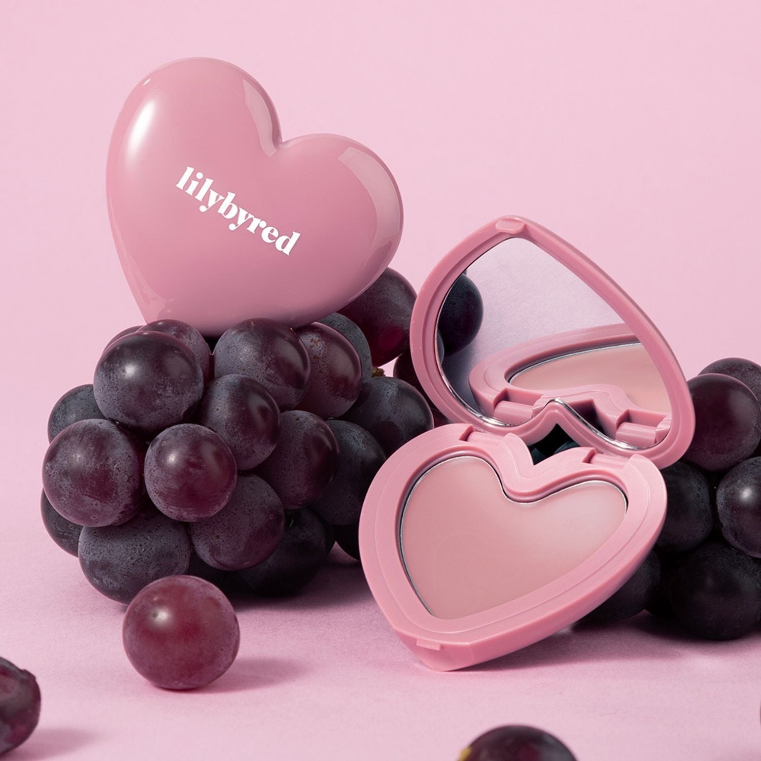 LILYBYRED Love Beam Cheek Balm de la marque LILYBYRED, présenté en forme de cœur rose sur fond rose avec raisins