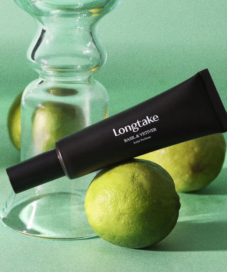 LONGTAKE Solid Perfume 30ml de LONGTAKE : tube noir et agrume sur fond vert, contexte visuel studio.