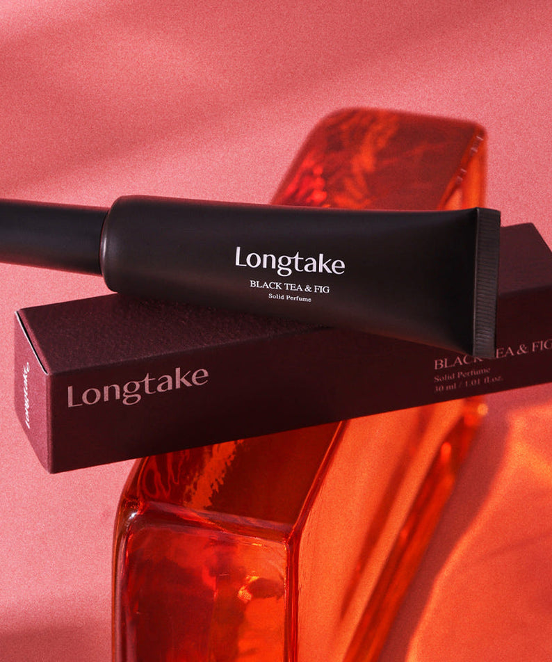 LONGTAKE Solid Perfume 30ml : tube et étui sur fond rose, bouteille & figue, produit en contexte visuel.