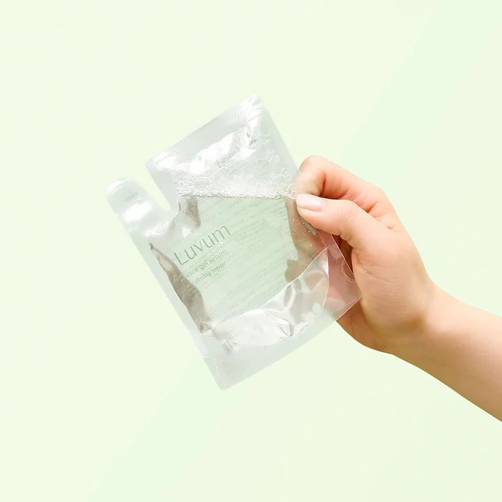 Main tenant LUVUM Calming Repair Cica Gel Serum Refill 80ml, pochette recharge, fond vert clair, soins réparateurs apaisants