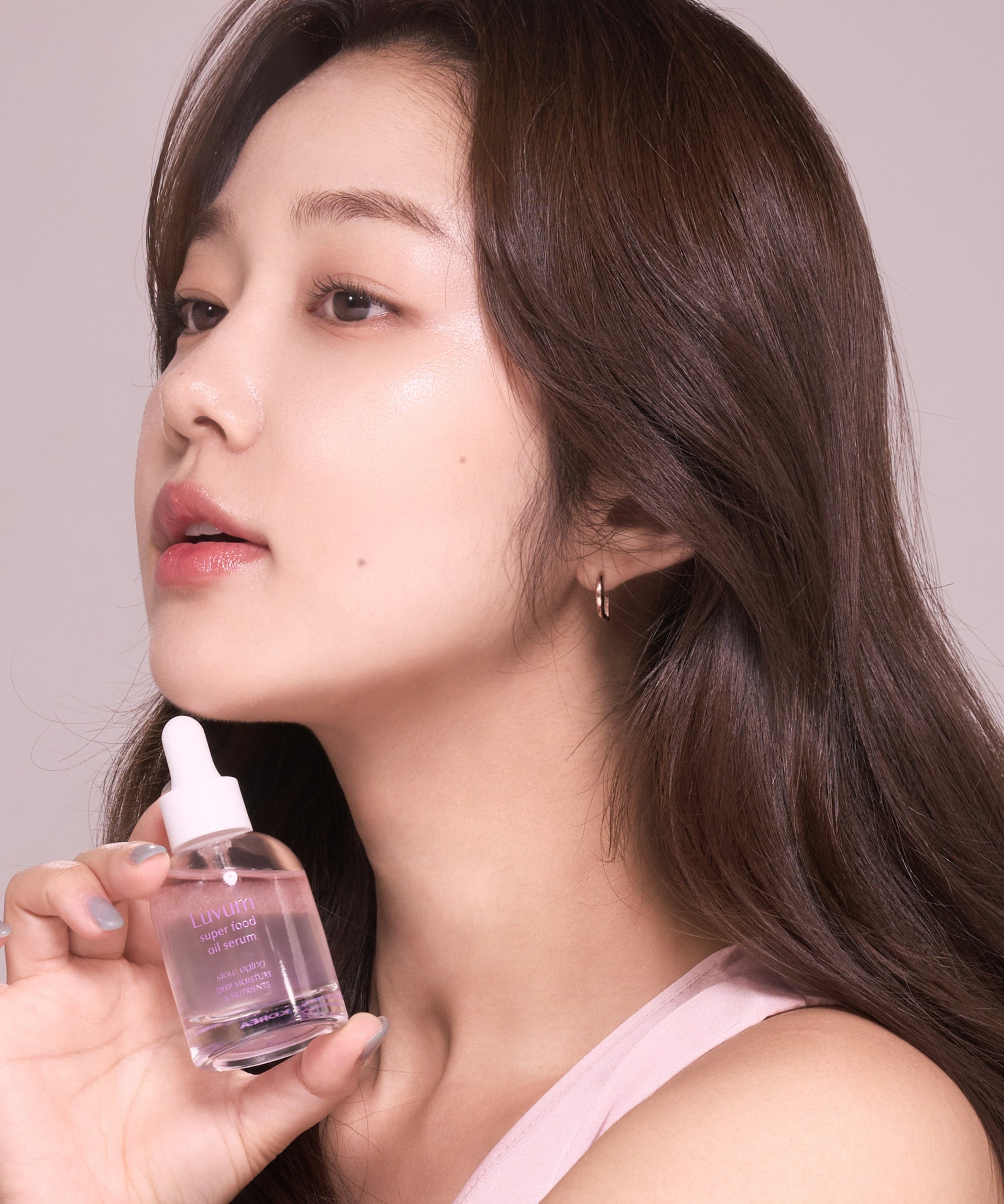LUVUM Slow Aging Super Food Oil Serum 30ml : la marque au visage, sérum à l’huile sur fond rose, main tenant le flacon.