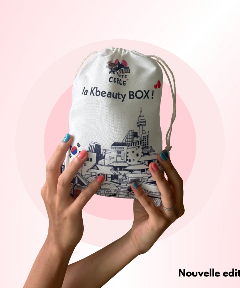 La K-beauty Box - Nouvelle edition : mains tenant un sac La Beauté Corée sur fond rose, visuel produit lifestyle.