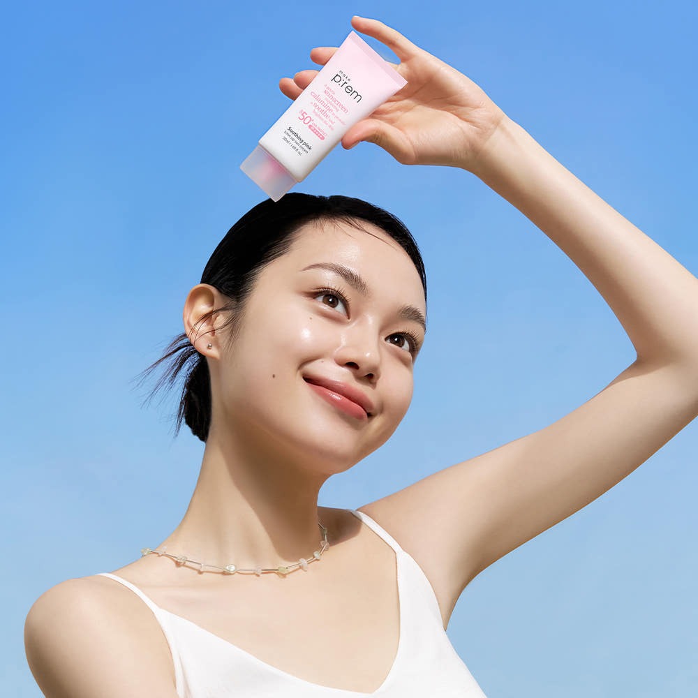 MAKE P:REM  Soothing Pink Tone-Up Sunscreen SPF 50+ PA++++ 50ml sur visage, main tenant le tube, fond ciel bleu