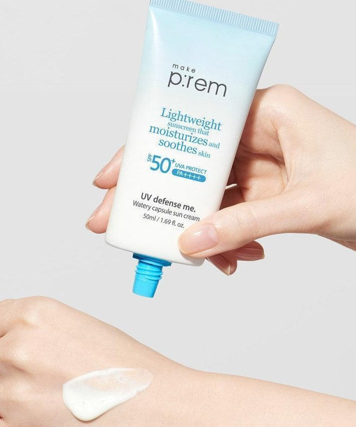 MAKE P:REM  UV Defense Me Watery Capsule Sunscreen 50ml SPF50+ PA++++, main tenant le tube bleu sur peau, fond clair.