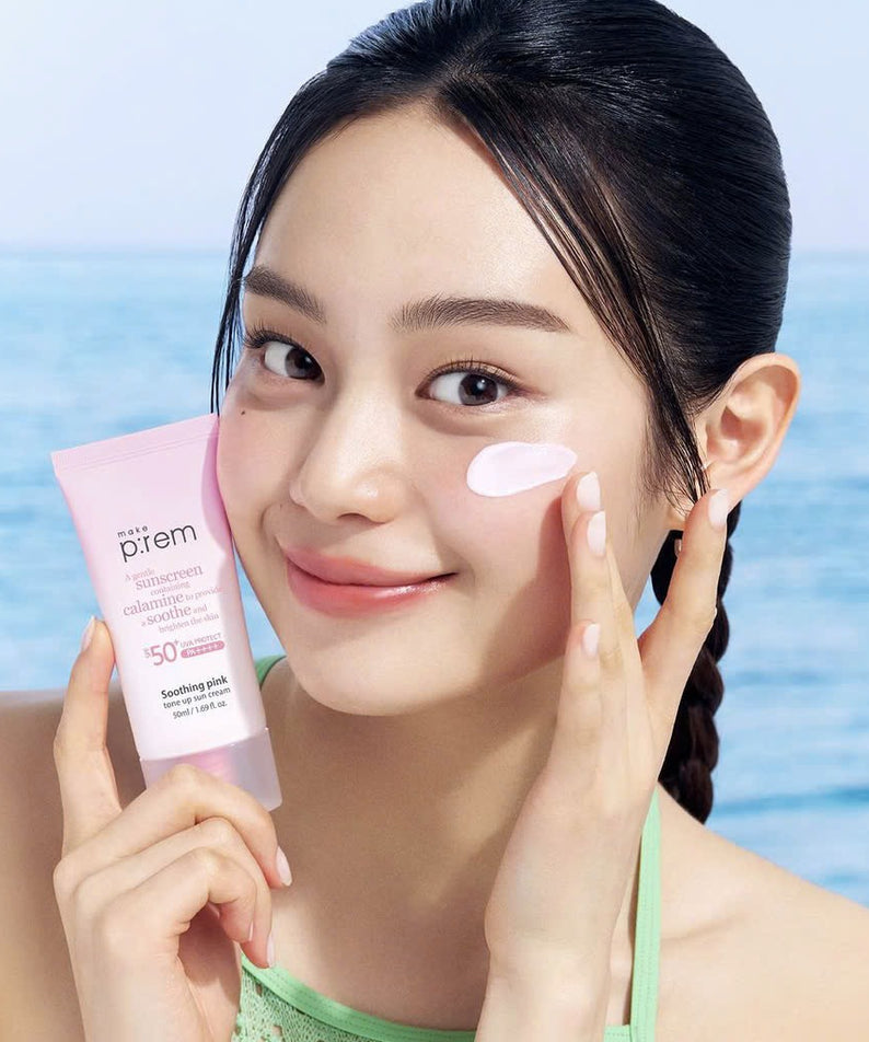 Femme appliquant MAKE P:REM Soothing Pink Tone-Up Sunscreen SPF 50+ PA++++ 50ml sur sa joue, montrant la texture du produit.