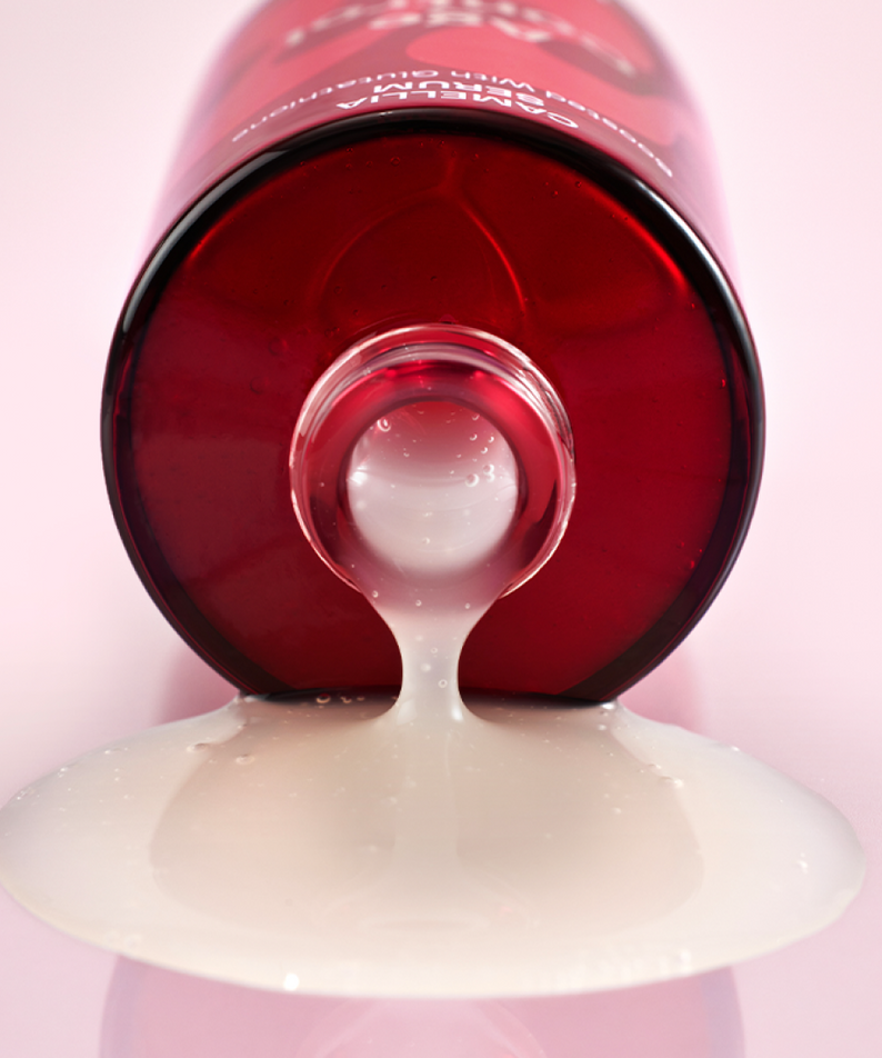 MAMONDE Age Control Camellia Serum 50ml se répandant d'une bouteille rouge sur fond rose, soin anti-âge hydratant luxe.