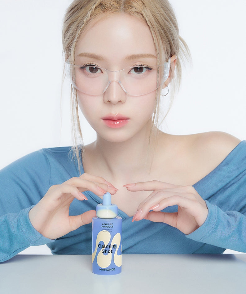 Femme tenant un flacon de MAMONDE Calming Shot Azulene Trace Moisture Ampoule 50ml avec une tenue bleue et lunettes de protection.