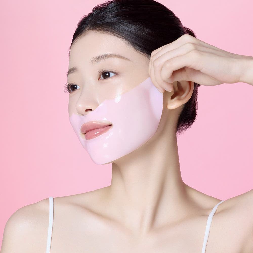 MAMONDE Flora Glow Rose Hydrogel Mask 1 sheet, marque MAMONDE : masque rose en gel sur visage, main pose la feuille, fond rose.