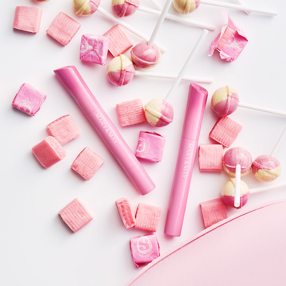 Décris l’image en français : MARY&MAY Blooming Glow Lip 09 Sunset Tangerine 1.7g, lèvres roses, bonbons sur fond clair.