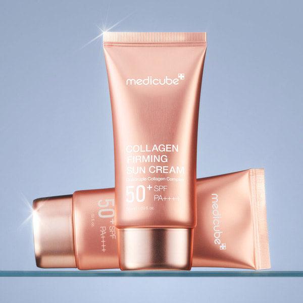 Décris l'image en français : MEDICUBE Collagen Firming Sun Cream 50ml, tube medocube sur fond bleu, éclats de lumière.