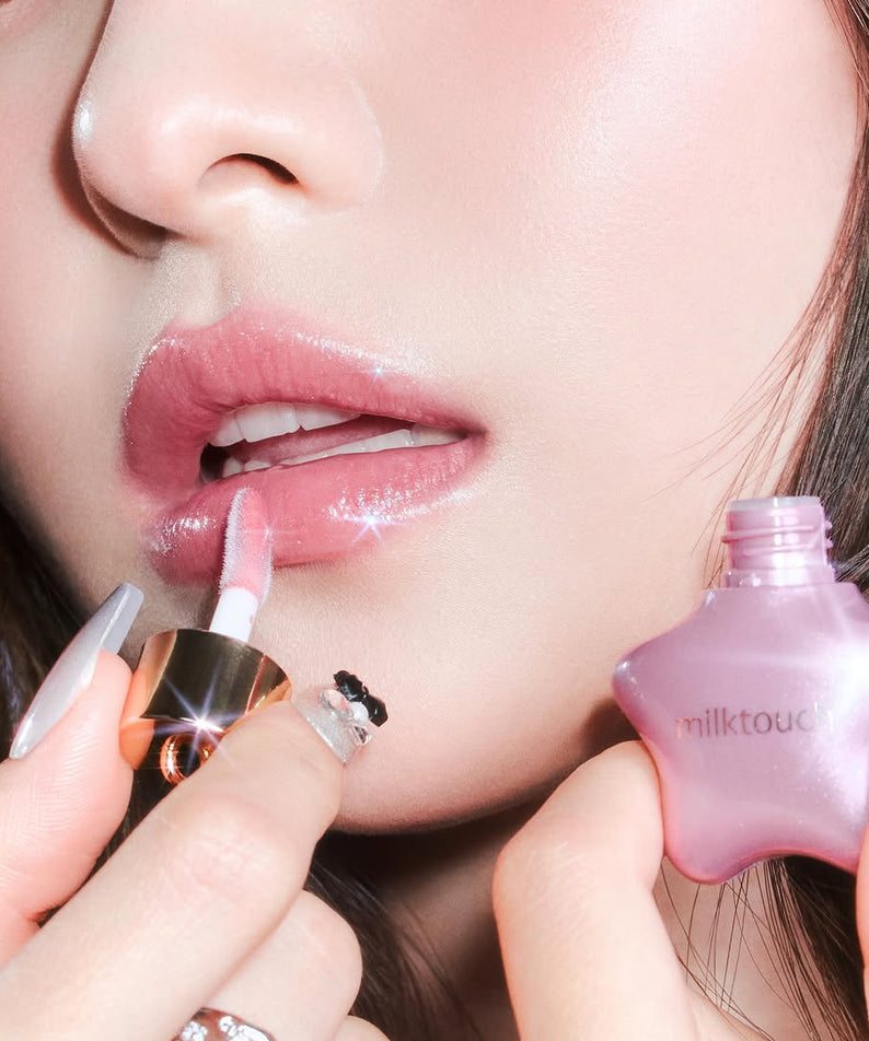 MILK TOUCH Ornament Prism Shine Pearl Gloss : lèvre nacrée rosée, flacon milk touch rose en contexte beauté maquillage, gros plan.