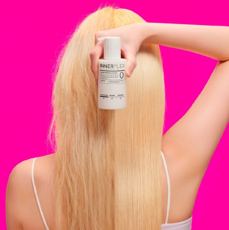 MISE EN SCENE Innerplex Hair Strengthening Shampoo 375g : flacon sur cheveux blonds, tenue par une main, fond rose.