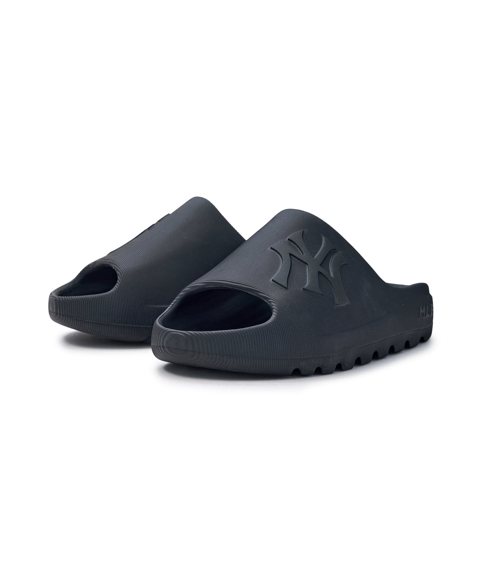 Décris l'image en français : MLB Skipper Slide New York Yankees BLACK, sandales noires avec logo NY, fond blanc.