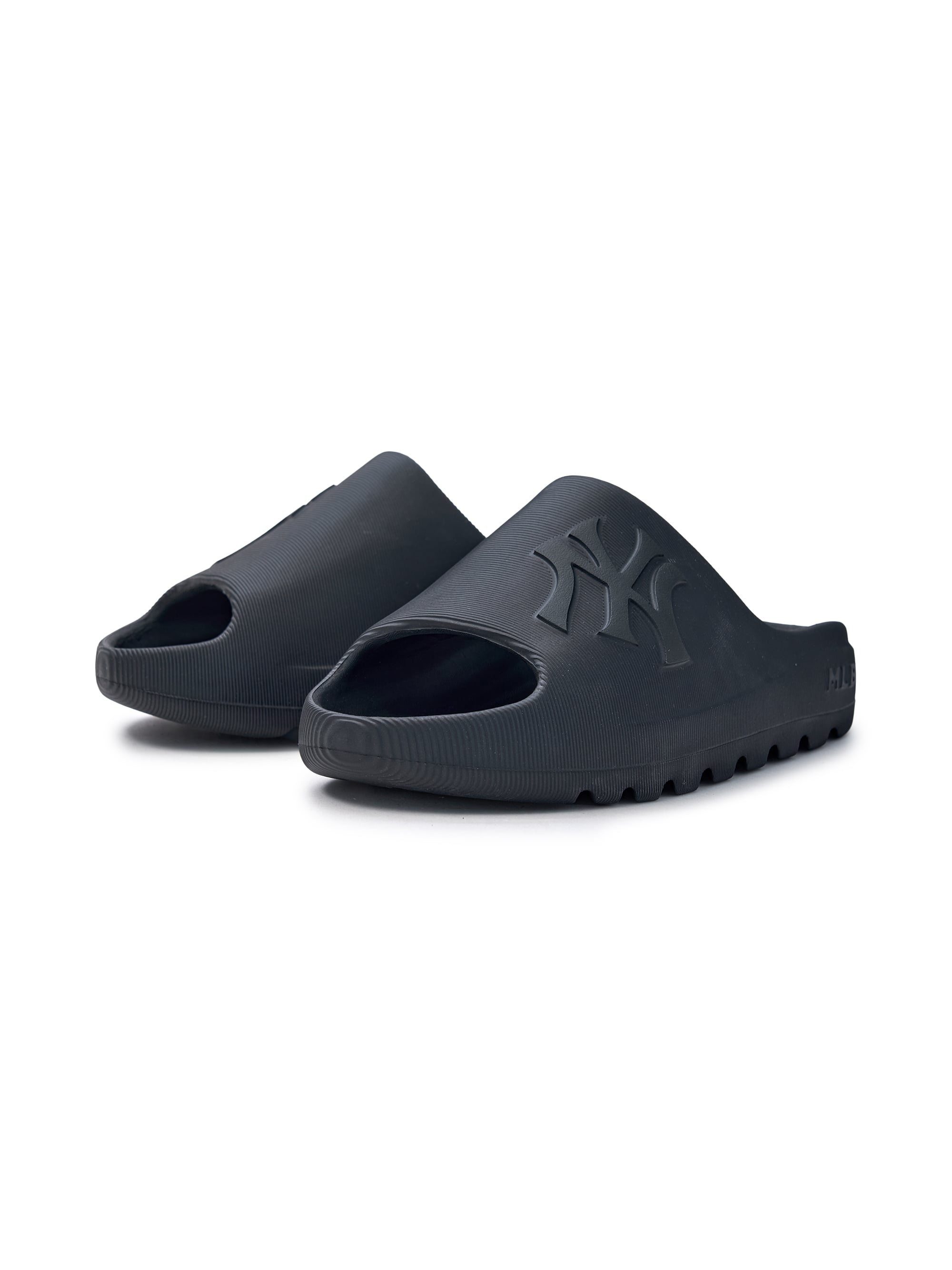 Décris l'image en français : MLB Skipper Slide New York Yankees BLACK, sandales noires avec logo NY, fond blanc.