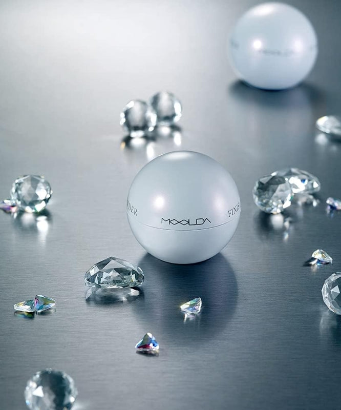 MOOLDA Water Finish Powder sur fond métallique avec cristaux étincelants en arrière-plan.