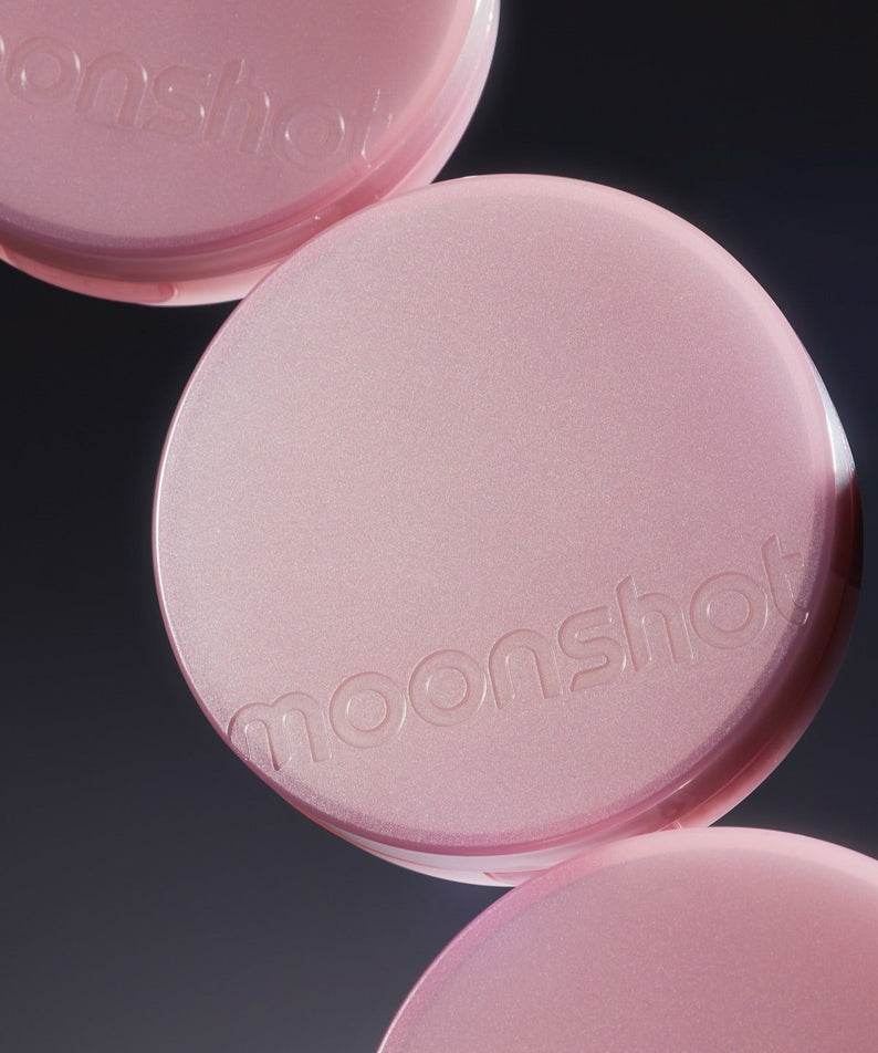 Décris l'image en français : MOONSHOT Conscious Fit Cushion Foundation Pink Moon Edition, boîtiers roses sur fond noir.
