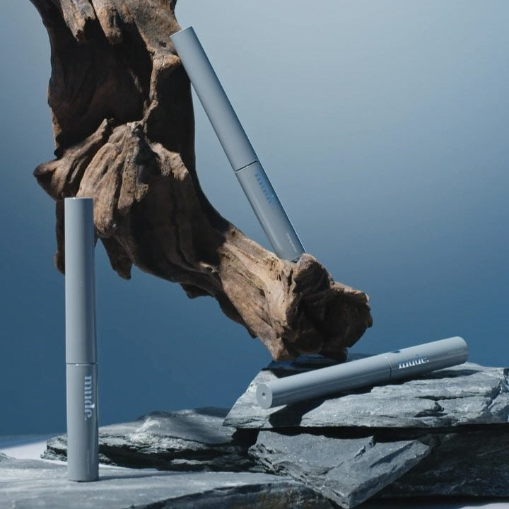 MUDE Eye Eye Ting Ting Serum Shot, flacon bleu MUDE sur rocher et fond ciel bleu, ambiance nature.