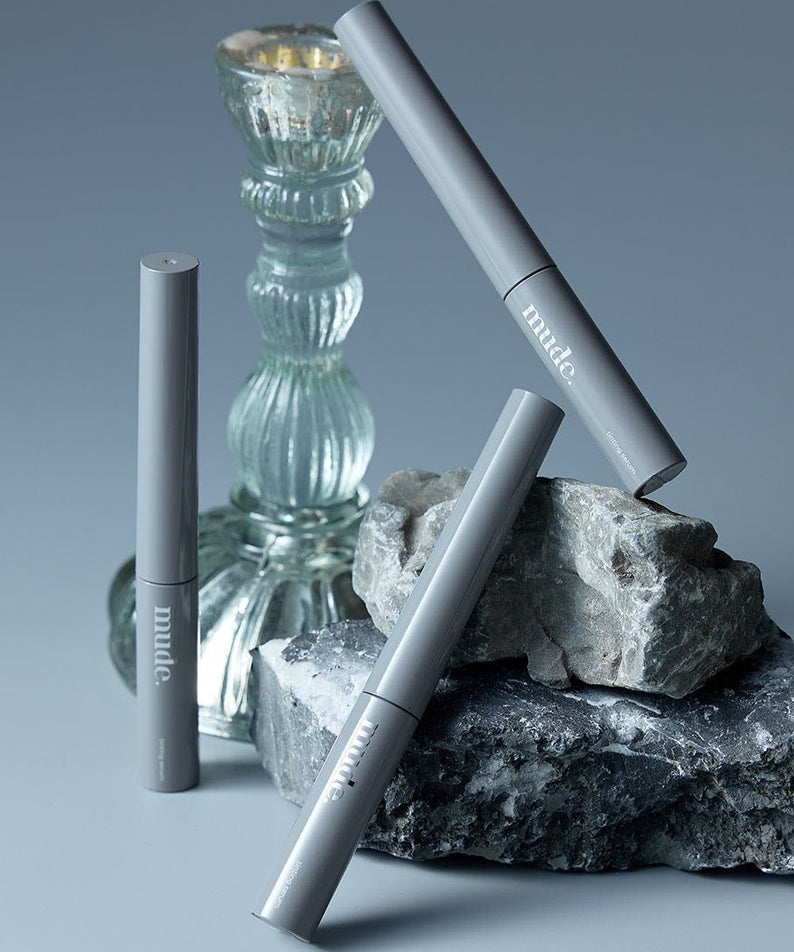 Sérum MUDE Eye Eye Ting Ting Serum Shot posé sur des roches avec bougeoir en verre en arrière-plan, ambiance élégante et sereine.