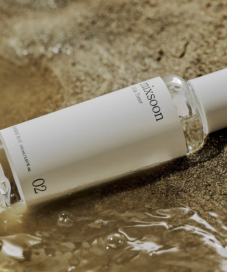 Mixsoon Centella Asiatica Toner 150ml, bouteille sur sable et eau, pack skincare apaisant en contexte naturel