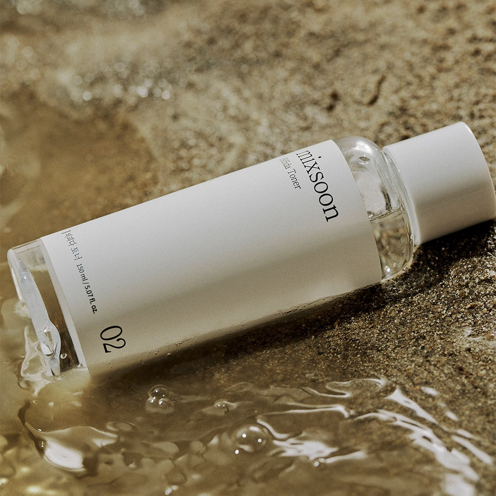 Mixsoon Centella Asiatica Toner 150ml, bouteille sur sable et eau, pack skincare apaisant en contexte naturel