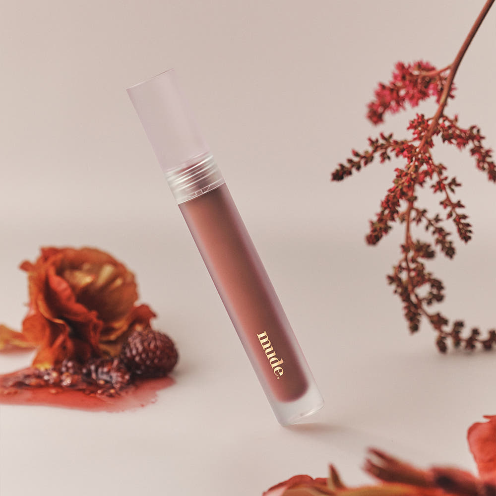 Mude Mood Soft Blur Tint, tube maquillage de la marque Mude, flou doux sur fond beige avec fleurs séchées.