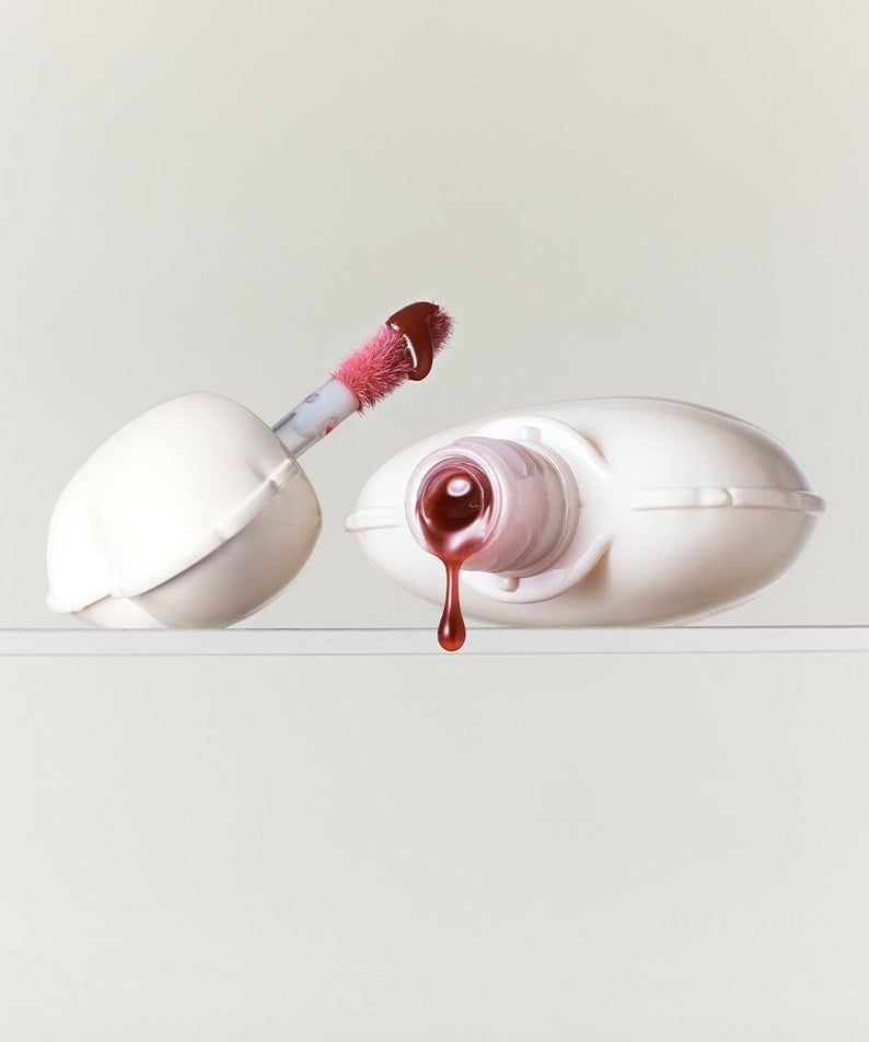 NAMING Glow Heart Lip Tint brun métallique sur fond blanc minimaliste, avec applicateur rouge tendre. Cosmétiques haut de gamme.