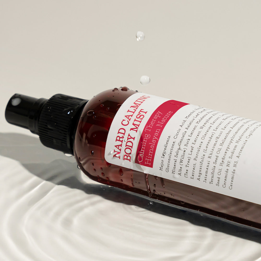 NARD Calming Body Mist 200ml : brume apaisante NARD sur tissu clair, flacon pulvérisateur, contexte beauté spa.